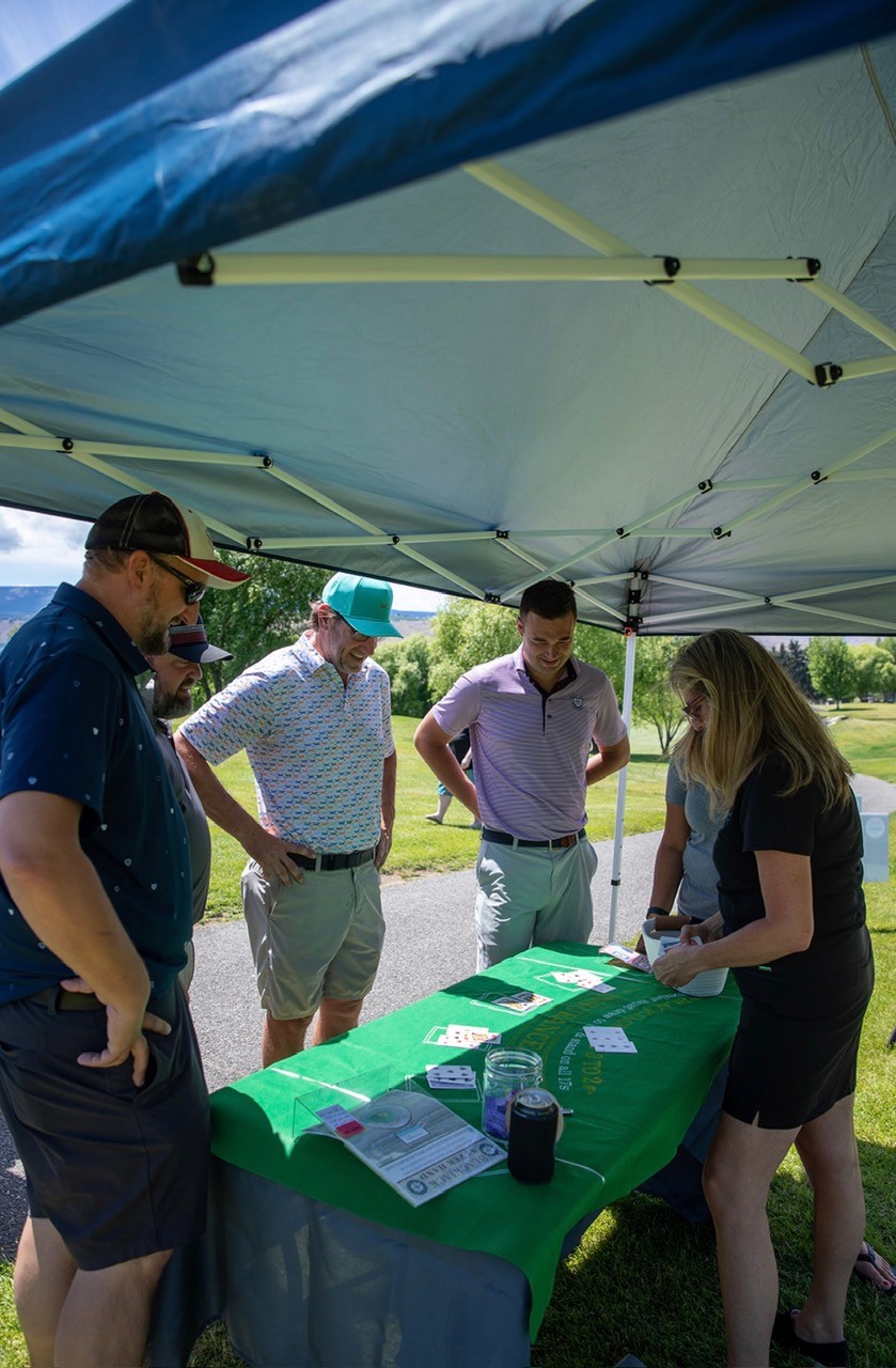 Players gathered around the card game table under a canopy at the Summer Golf Tournament
